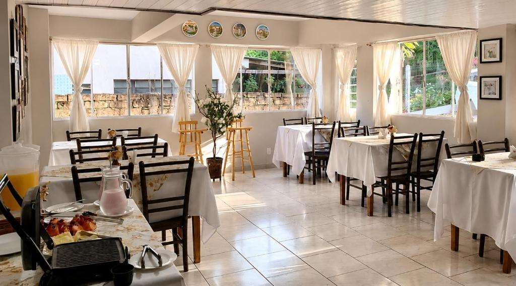 Salão do café da manhã da Pousada Folhas de Outono, com mesas de toalha branca e janelas com cortinas