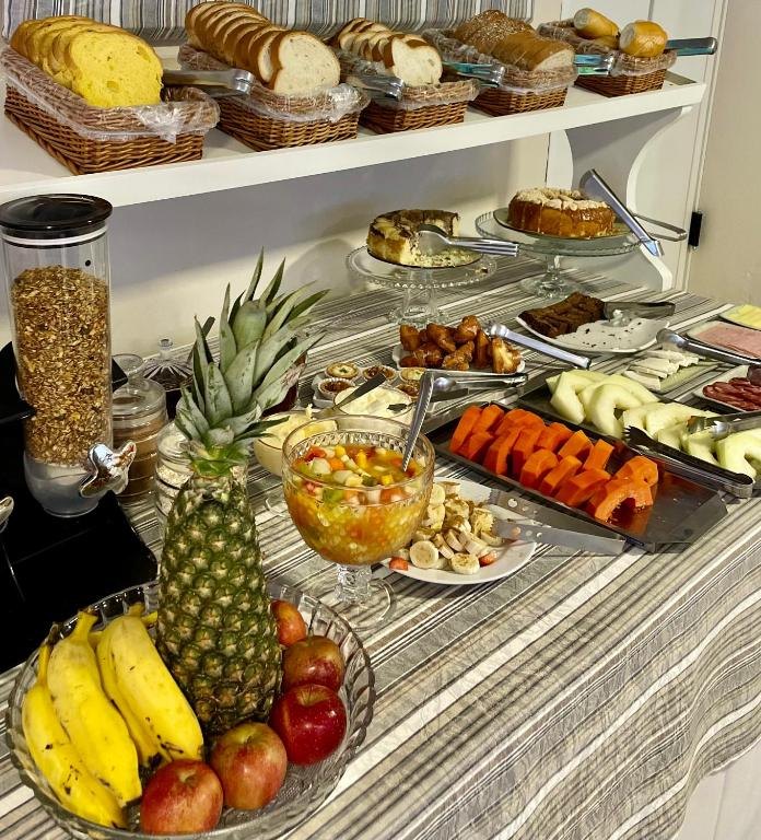 Mesa do café da manhã, com cestas de pães, bolos, frutas, frios e salada de frutas