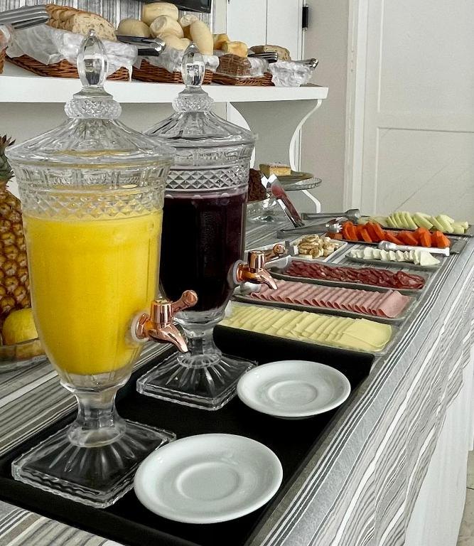 Jarras de suco de laranja e de uva sobre a mesa do café, ao lado de frios e frutas
