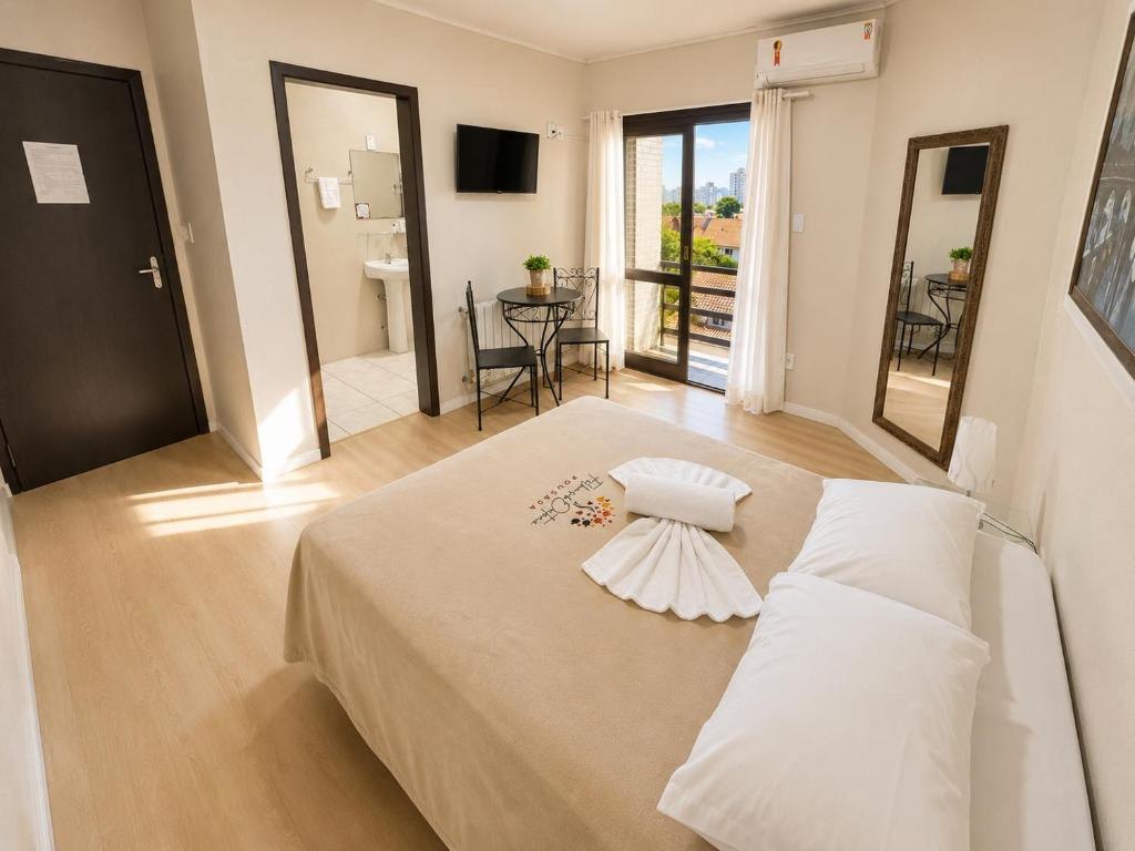 Quarto Casal da Pousada Folhas de Outono, com cama de casal, mesa com duas cadeiras, espelho, ar-condicionado e varanda